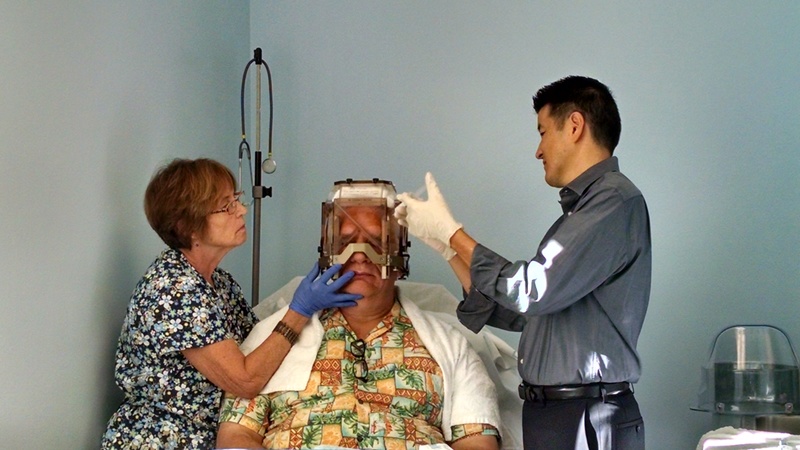 The nurse holds the frame so it will not rest on my nose. The doctor injects novocain (I think) to numb my scalp where the bolts will go in.