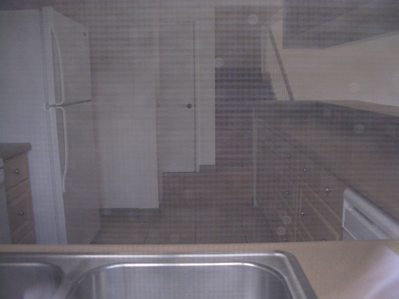 Looking in the kitchen window. You can see the sink, fridge, closet under the stairs, and stairway.